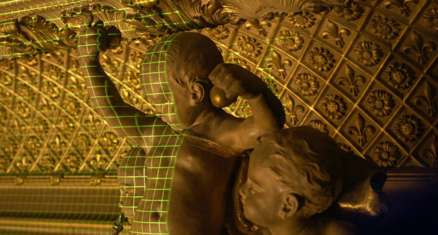 Vluks Media Argentina - IP - ND - Noticiario Digital Bronze sculpture of two figures in a dramatic pose, with a green grid overlay on one body, set against an ornate patterned ceiling.